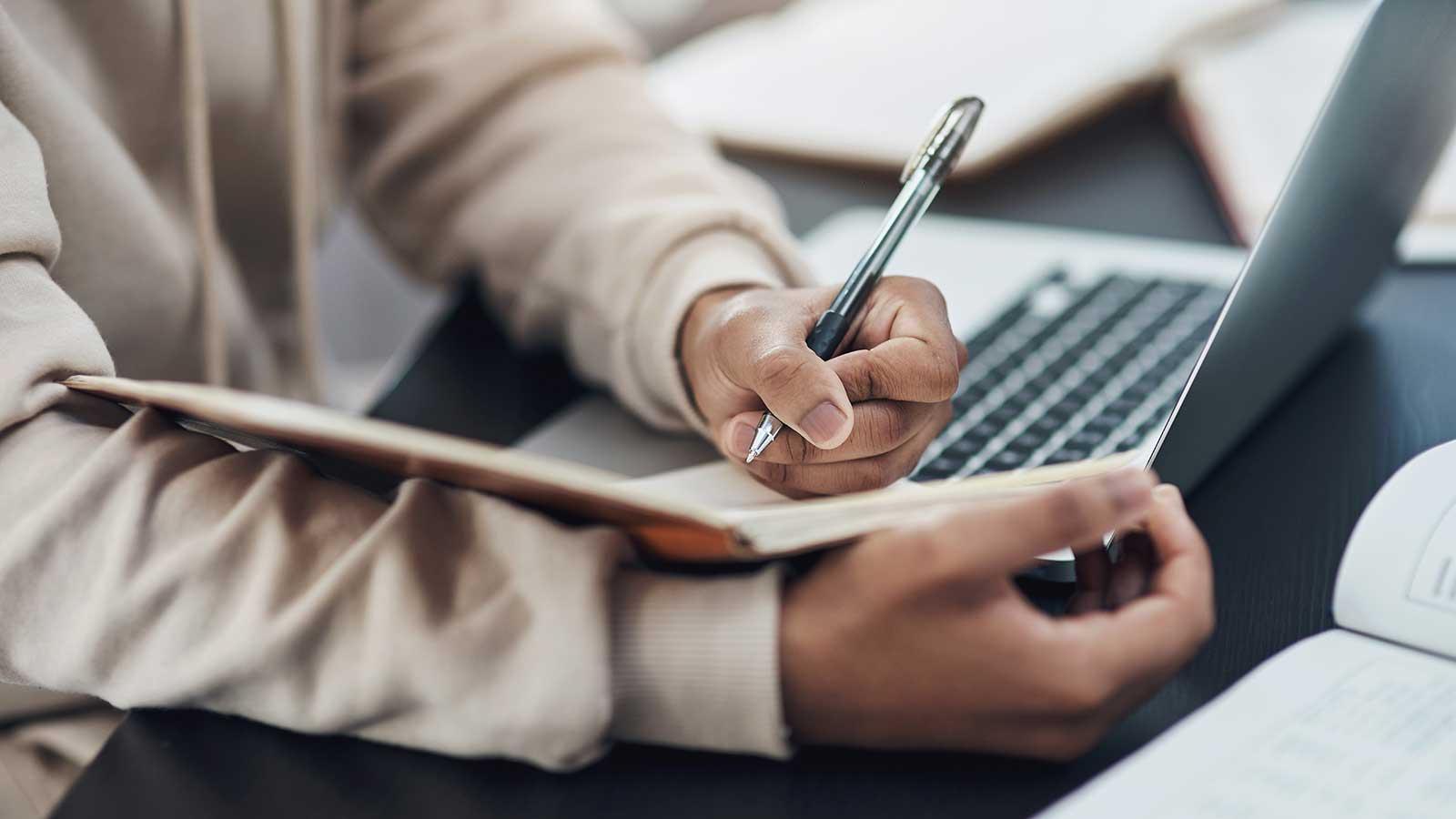 Person taking notes from laptop representing Business Studies program at Clarkson